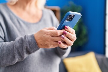 Middle age blonde woman using smartphone standing at home