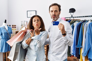 Obraz premium Hispanic middle age couple holding shopping bags and credit card looking at the camera blowing a kiss with hand on air being lovely and sexy. love expression.