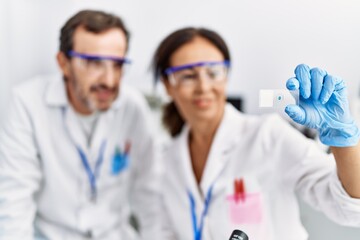 Middle age man and woman partners wearing scientist uniform analyzing sample at laboratory