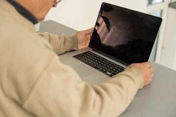 Senior man with eyeglasses connected with laptop at home.
