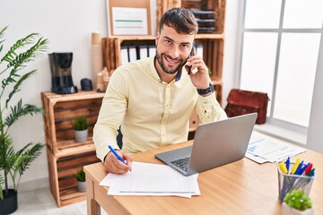 Naklejka premium Young hispanic man business worker talking on the smartphone working at office