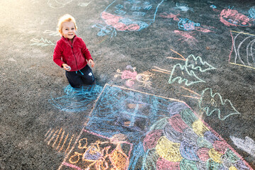 Happy little girl draws with chalk on asphalt. Kid’s creativity.