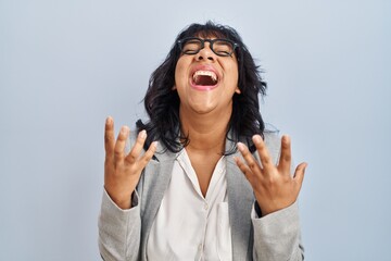 Hispanic woman standing over isolated background crazy and mad shouting and yelling with aggressive expression and arms raised. frustration concept.