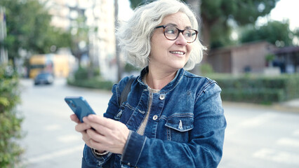 Fototapeta premium Middle age woman with grey hair using smartphone at park