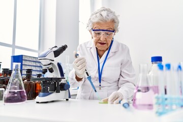 Senior grey-haired woman wearing scientist uniform using pipette at laboratory