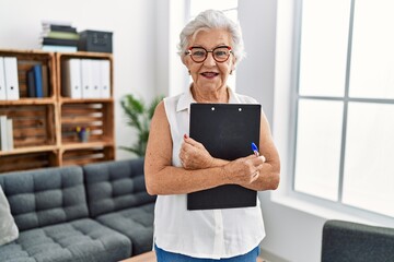 Senior grey-haired woman psychologist holding clipboard at psychology center