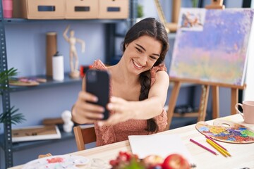 Fototapeta premium Young hispanic woman artist drawing on notebook make selfie by smartphone at art studio
