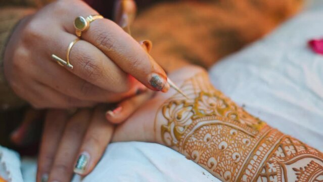 Close up shot of Mehndi artist drawing beautiful mehndi in Indian bride's hand on occasion of wedding in India. Artist making mehndi in bridal hand in Gujarat, India. Celebrating Indian wedding 