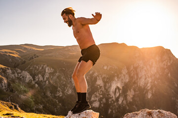 Man doing conditioning training on top of a mountain in the early morning with the sunrise in the background