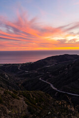 Sun setting horizon and mountains. Photo taken from a lookout in the Santa Monica mountains in Malibu. Headlights and taillights of cars in traffic are seen on the meandering and scenic PCH