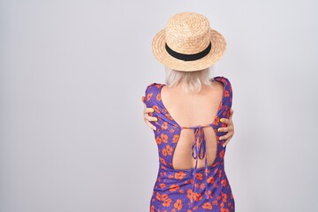 Young caucasian woman wearing flowers dress and summer hat hugging oneself happy and positive from...