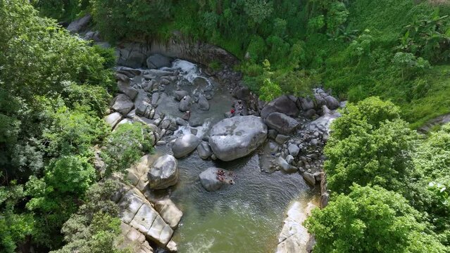 Veiws of a mountain river pool at the bottom of a Puerto Rican rainforest, with people enjoying the afternoon. 