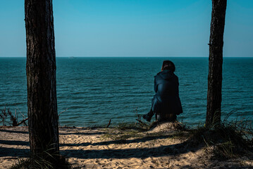 A lonely woman sitting between trees and watching to a calm and silent see meditating