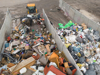 Yellow skid steer loader moving wooden waste material, shaking out a scrap grapple on the garbage...