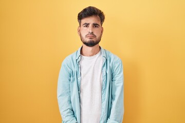 Young hispanic man with tattoos standing over yellow background depressed and worry for distress, crying angry and afraid. sad expression.