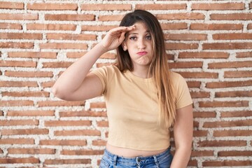 Young brunette woman standing over bricks wall worried and stressed about a problem with hand on forehead, nervous and anxious for crisis