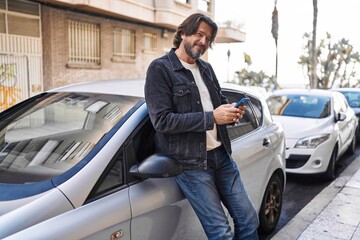 Middle age man using smartphone leaning on car at street