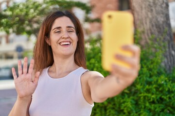 Brunette woman taking a selfie photo with smartphone looking positive and happy standing and smiling with a confident smile showing teeth