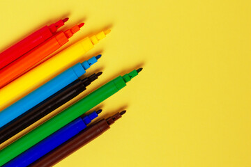 Felt-tip pens without caps of different colors on a yellow background.