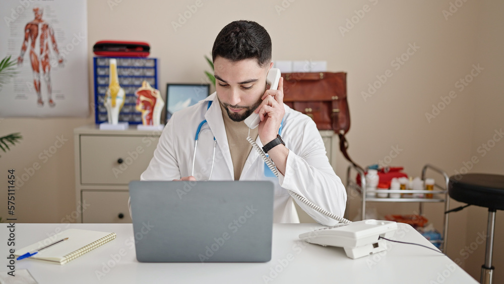 Sticker Young arab man doctor using laptop talking on telephone at clinic