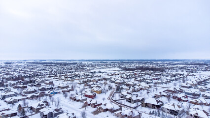 Aerial drone view of a snow covered suburban residential neighborhood with rows of white roofs and houses. 