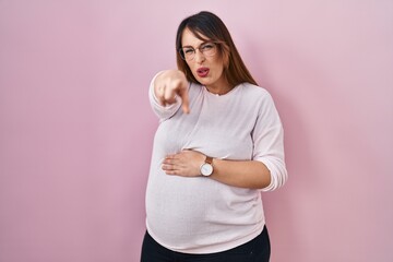 Pregnant woman standing over pink background pointing displeased and frustrated to the camera, angry and furious with you