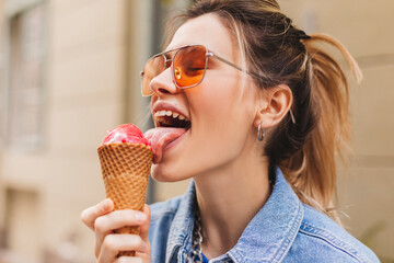 Close up portrait woman with high ponytail hold delicious pink ice cream in waffle cone outdoors....