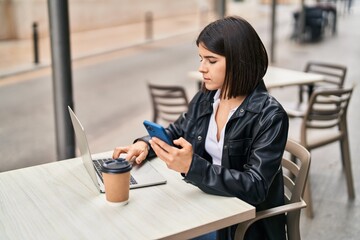 Fototapeta premium Young beautiful hispanic woman using smartphone sitting on table at coffee shop terrace