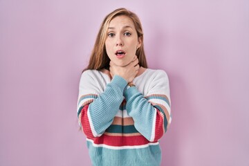 Young blonde woman standing over pink background shouting suffocate because painful strangle....