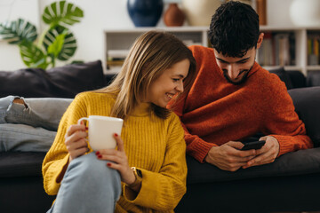 Caucasian man and woman are sitting in the living room and looking at the phone