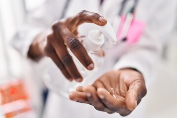 Obraz na płótnie Canvas African american woman wearing doctor uniform using sanitizer gel hands at clinic