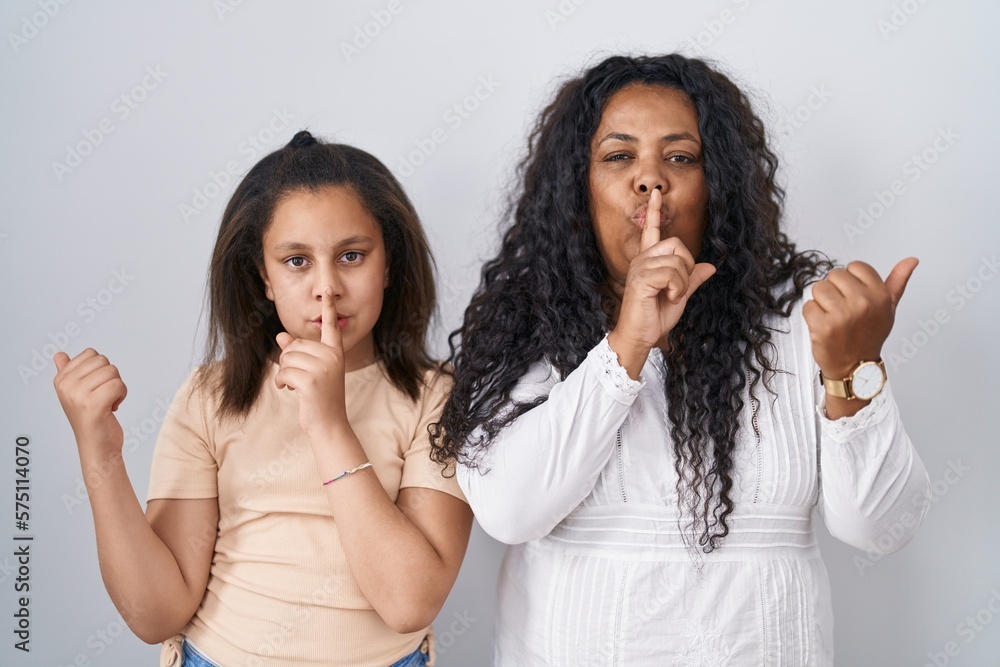 Sticker Mother and young daughter standing over white background asking to be quiet with finger on lips pointing with hand to the side. silence and secret concept.