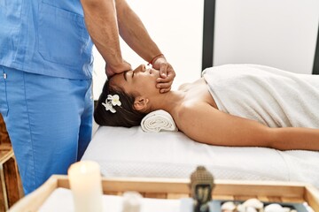 Obraz na płótnie Canvas Latin man and woman wearing physiotherapy uniform having rehab session massaging head at beauty center