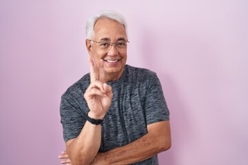 Middle age man with grey hair standing over pink background smiling with happy face winking at the...