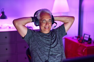 Middle age grey-haired man streamer smiling confident relaxed with hands on head at gaming room
