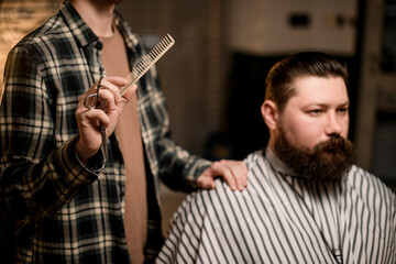 view on bearded man client and male barber with comb in his hand