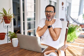 Fototapeta premium Middle age man using computer laptop at home shouting suffocate because painful strangle. health problem. asphyxiate and suicide concept.