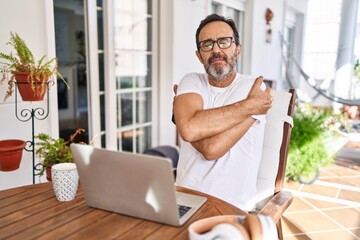 Middle age man using computer laptop at home hugging oneself happy and positive, smiling confident....