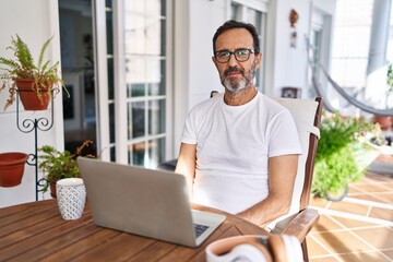 Middle age man using computer laptop at home relaxed with serious expression on face. simple and natural looking at the camera.