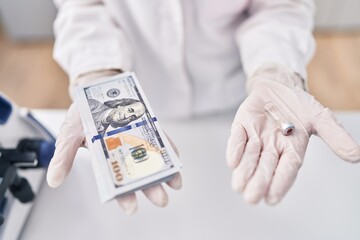Young woman scientist holding vaccine dose and dollars at laboratory