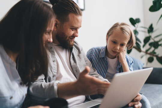 Happy father pointing at laptop screen showing photos to daughter