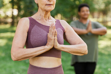 Cropped shot of senior woman enjoying yoga outdoors and holding hands together by chest in...