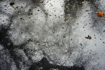 Nasse weiße Tischfläche mit brauen Laubblättern und schwarzer Baumreflexion bei Regen am...