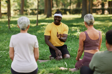 Naklejka premium Full length portrait of smiling yoga coach talking to group of senior women in outdoor workout