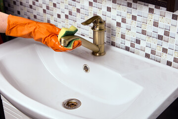 Maid is cleaning brass faucet in bathroom to remove limescale.