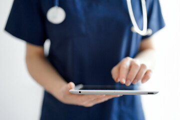 Doctor woman using tablet computer while standing near panorama window in clinic, close up. Physician or surgeon at work. Medicine concept