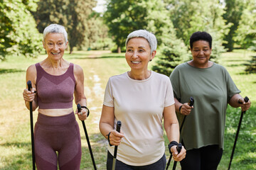 Group of active senior women walking with poles towards camera outdoors and smiling