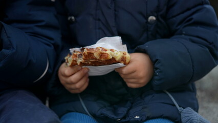 Small boy eating belgium street food outside during winter season. Children wearing coat snacking sweet dessert