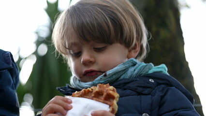Child taking a bite of Belgium Waffle outside during winter season