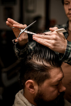 close-up of hands of barber holding strand of hair and scissors and masterfully do haircut